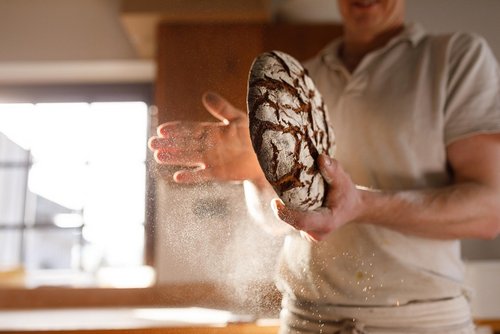 Bäcker der ein Krustenbrot in der Hand hält und das Mehl abklopft